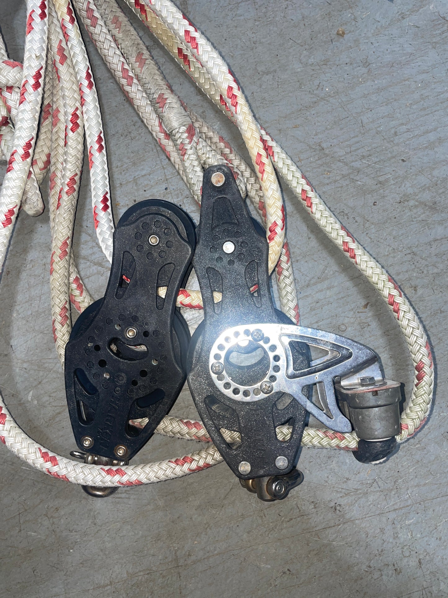 Black metal pulley system with red and white rope on a gray surface