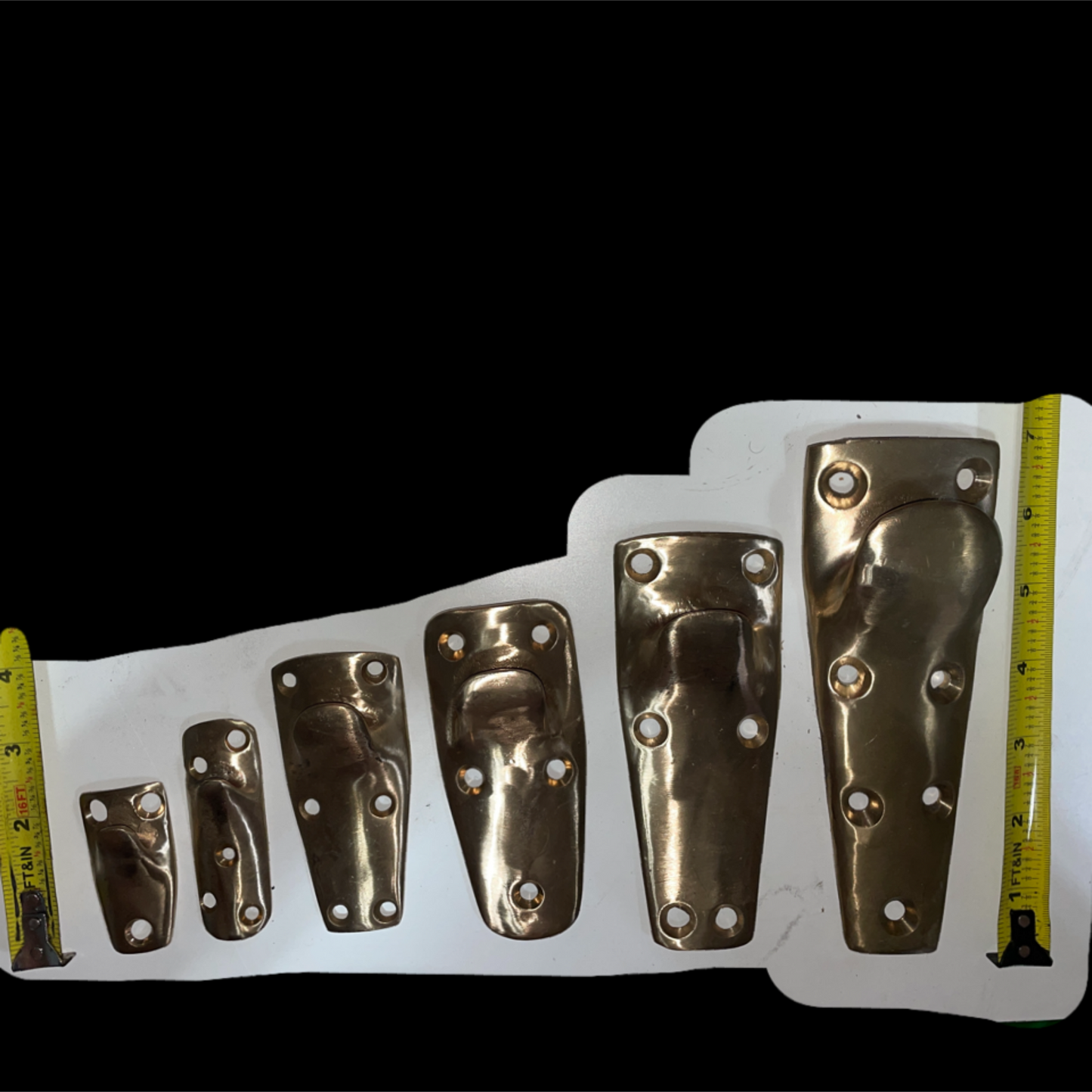 Set of brass brackets of different sizes on a white background with measurement tape for scale.