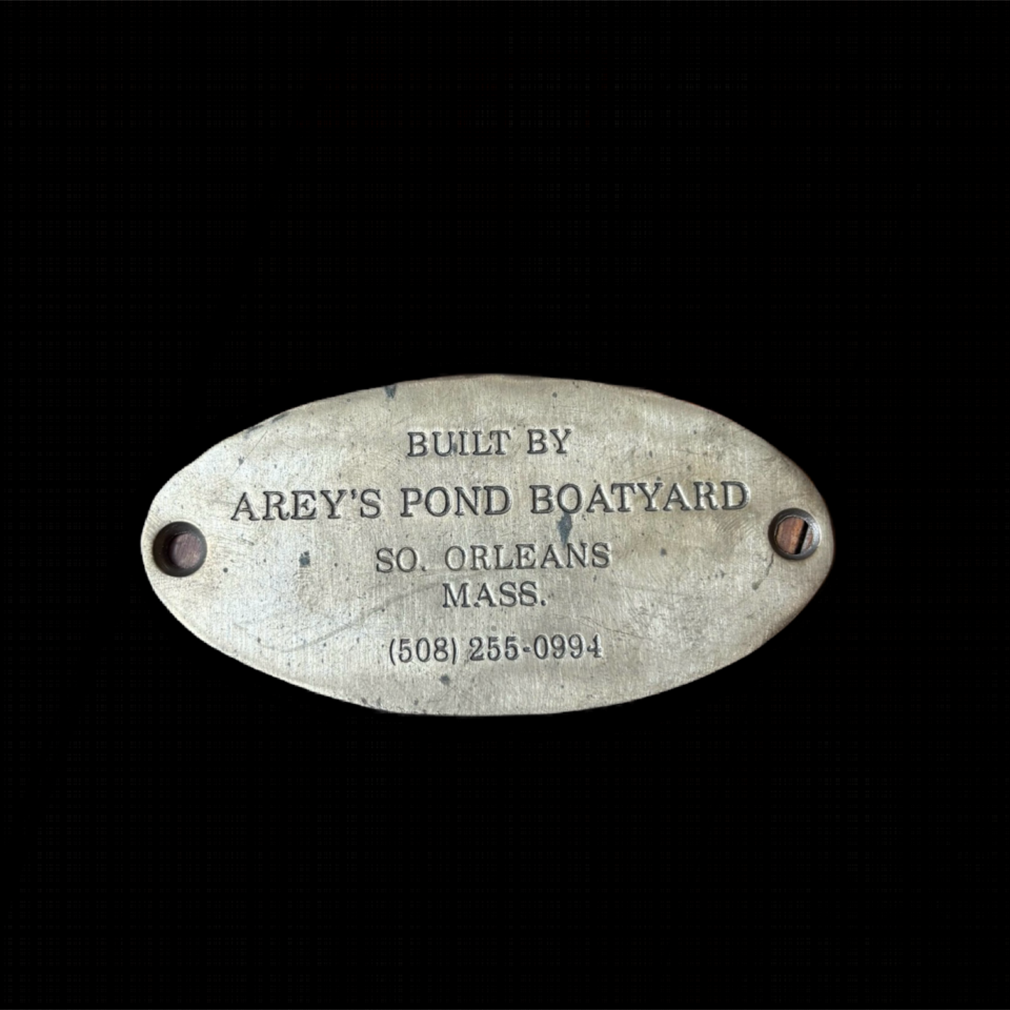 Metal plaque with text 'Built by Arey's Pond Boatyard, So. Orleans, Mass.' on a black background