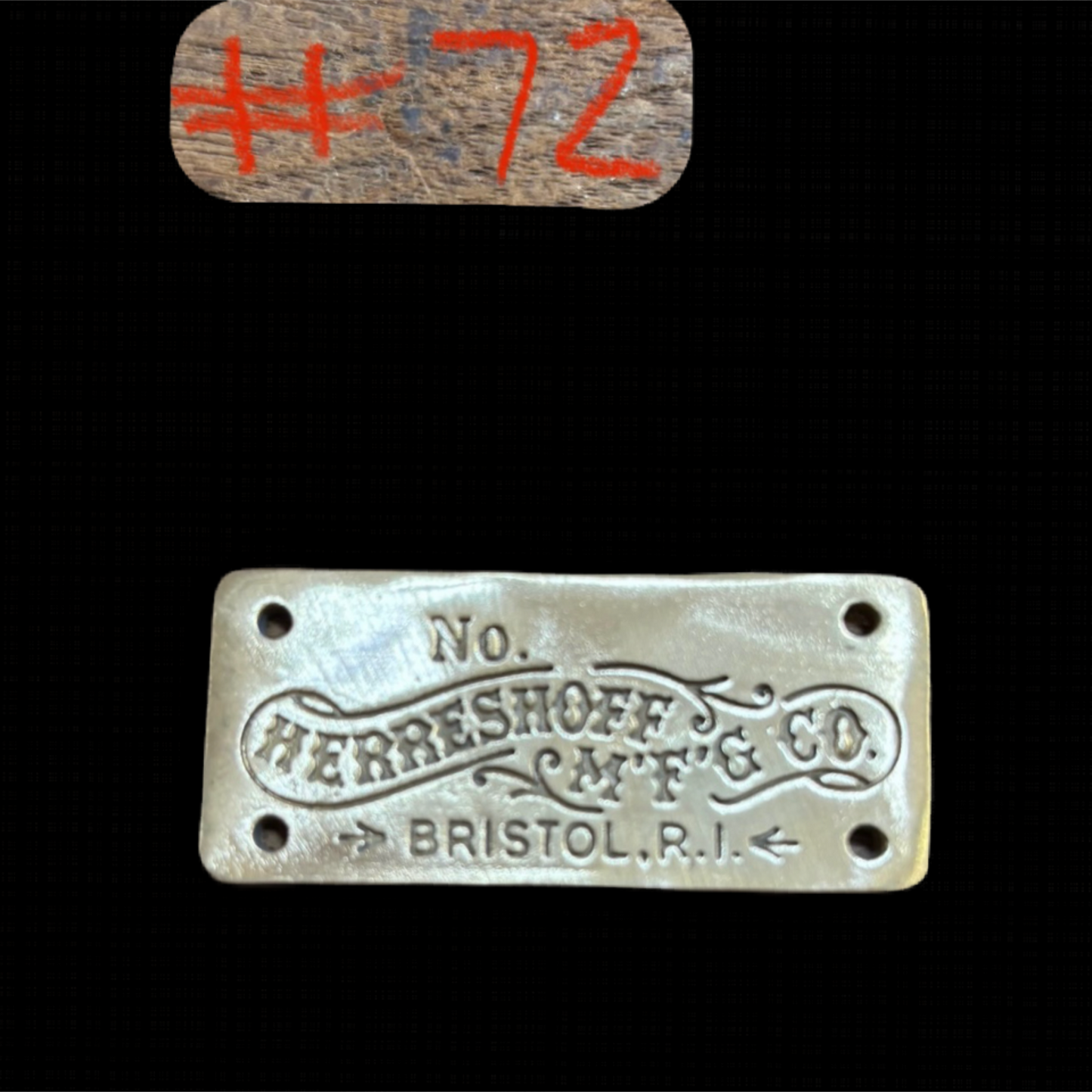 Metal tag with 'Herreshoff Mfg & Co' branding and '#72' marking on a black background