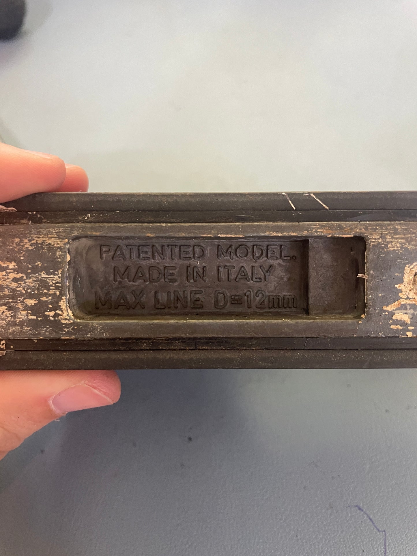 Vintage tool with 'Patented Model Made in Italy' engraving held by a hand against a gray background