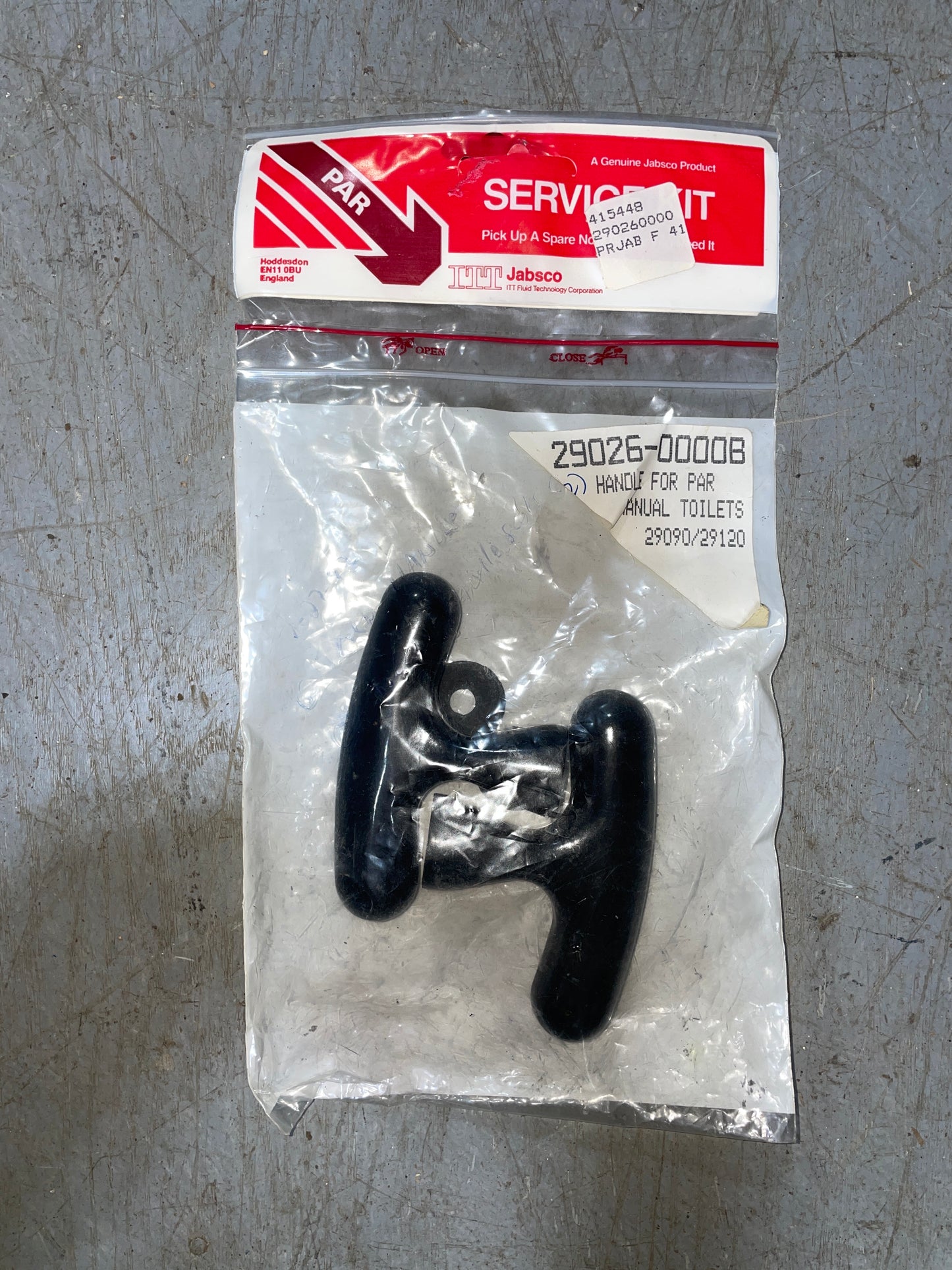 Black toilet handle in clear packaging with a red and white label on a gray surface
