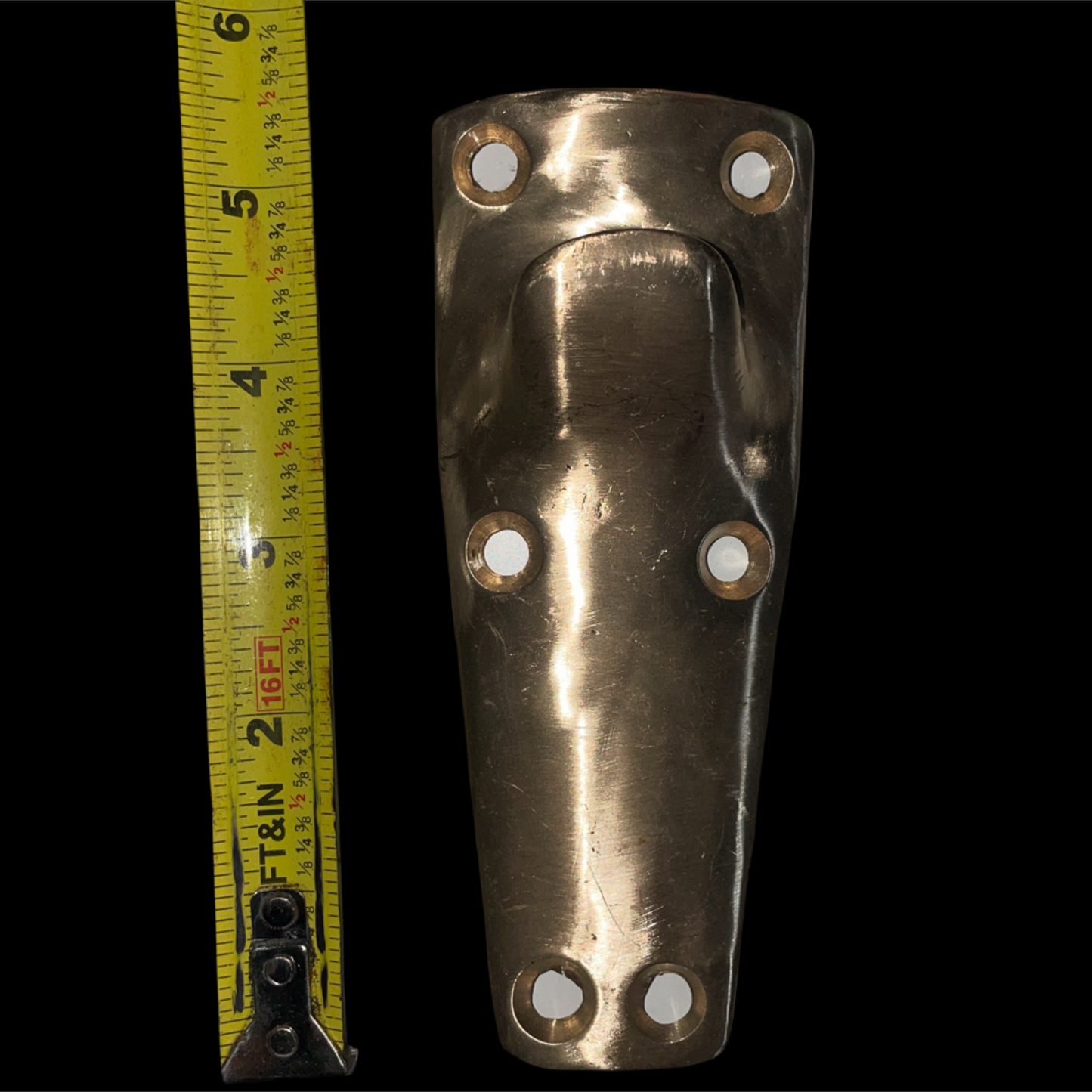 Brass fitting with holes next to a tape measure on a black background