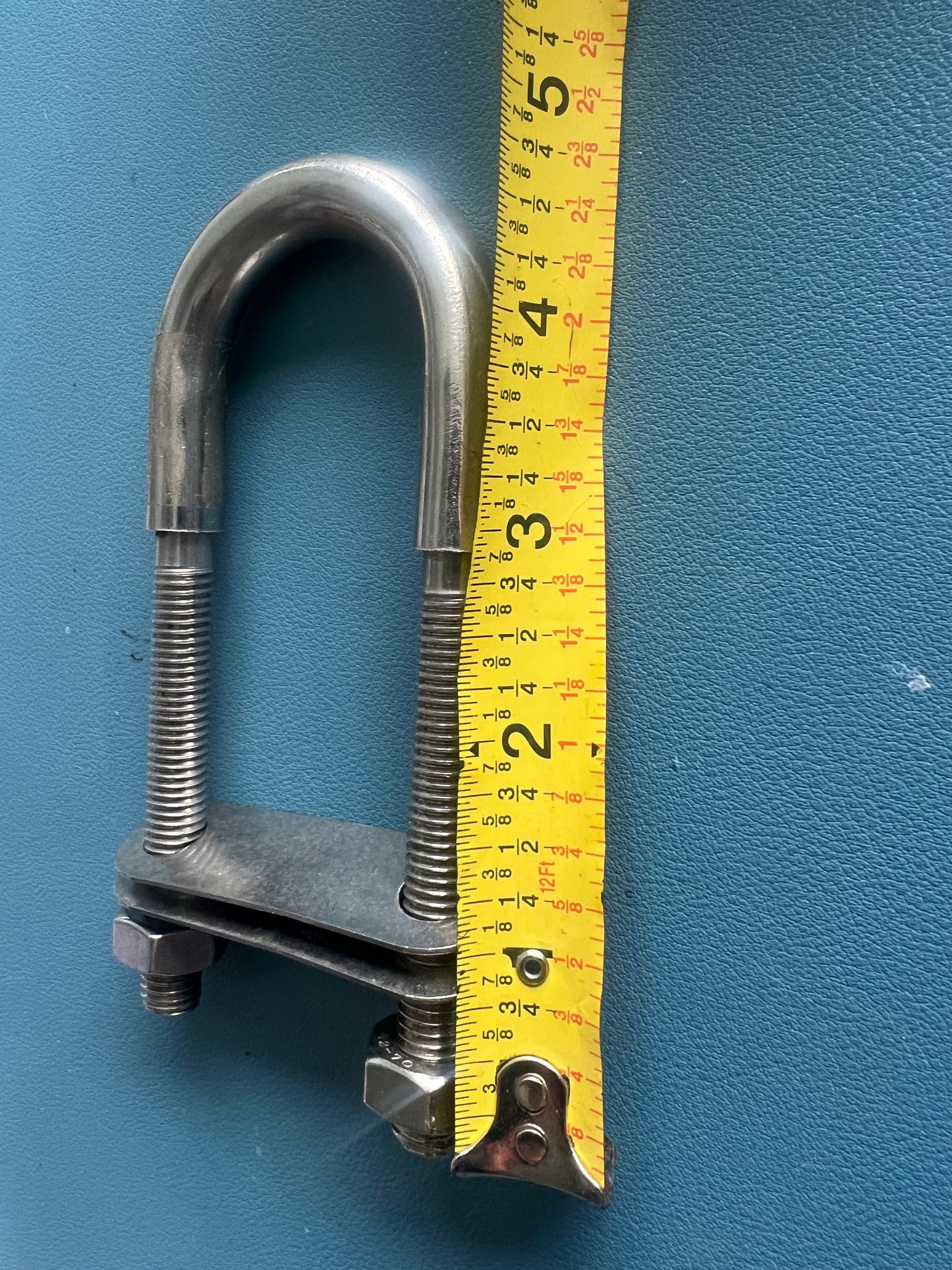 Metal U-bolt with nuts and a measuring tape on a blue background