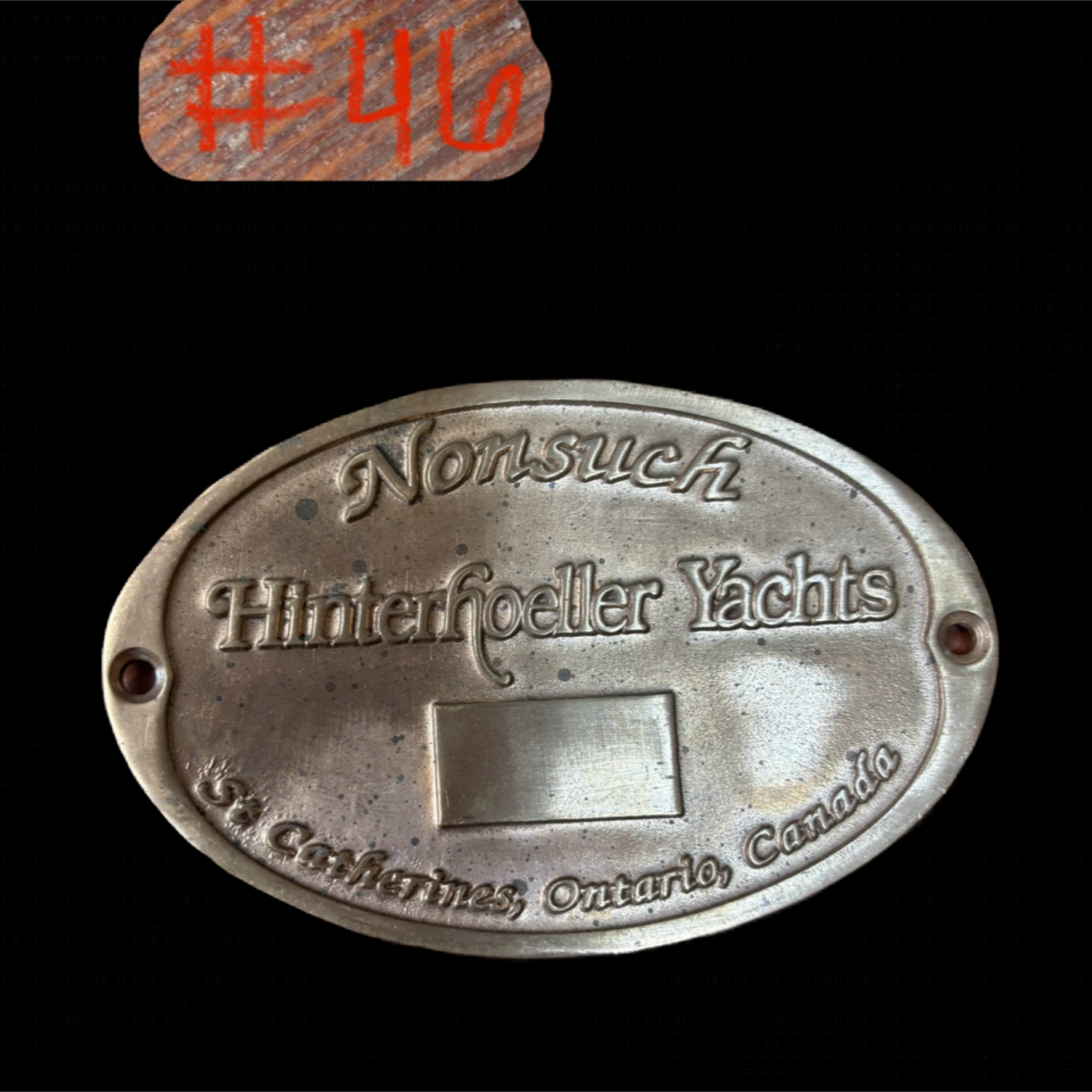 Metal plaque with 'Nonsuch Hinterhoeller Yachts' text on a black background