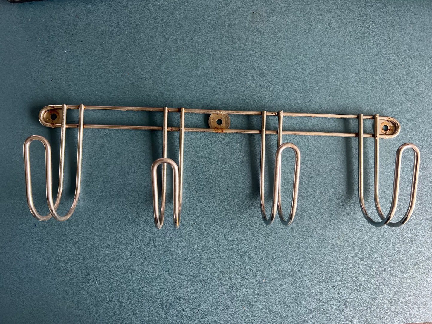 Metal wall-mounted rack with hooks on a blue background