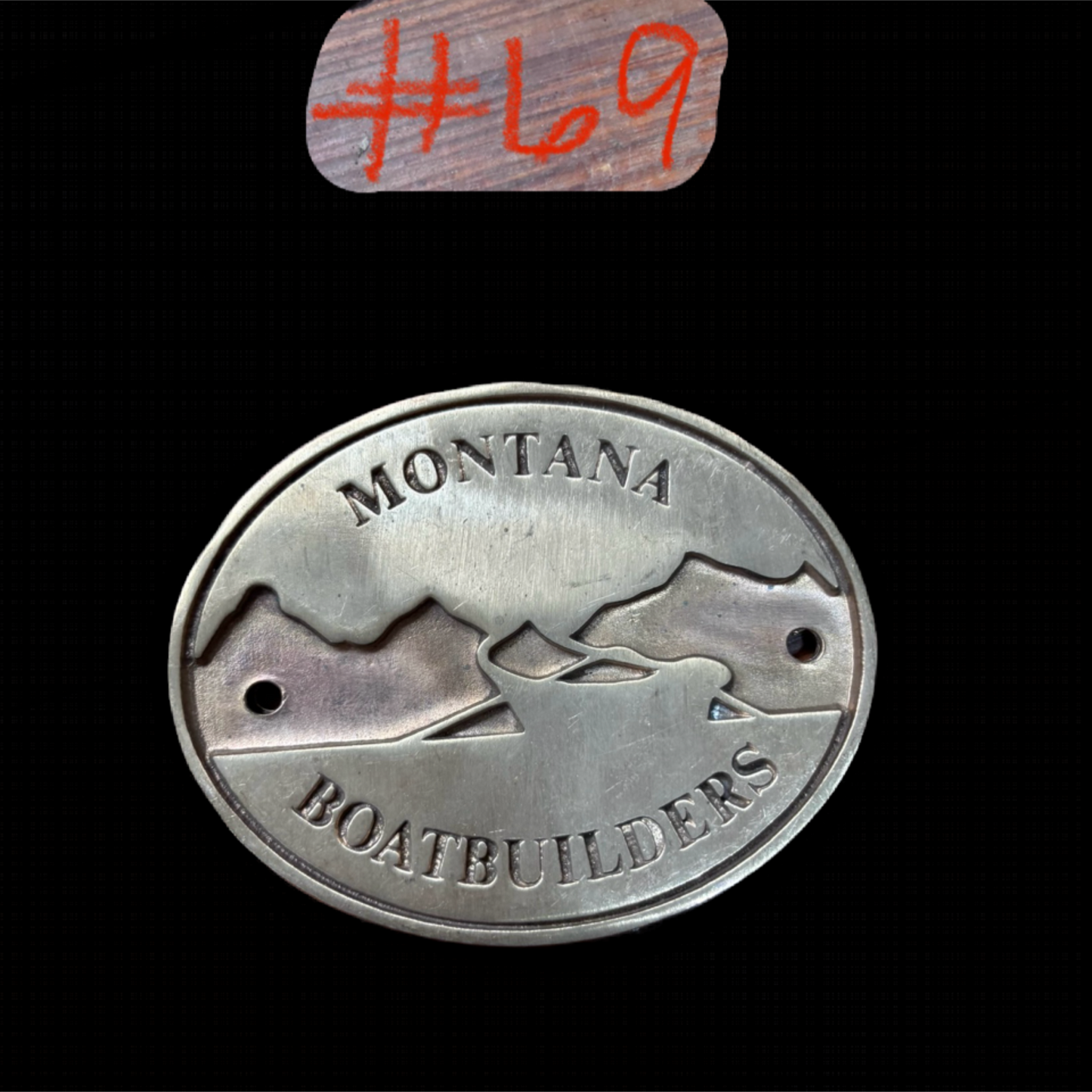 Metal badge with 'Montana Boatebuilders' text and mountain design on a black background