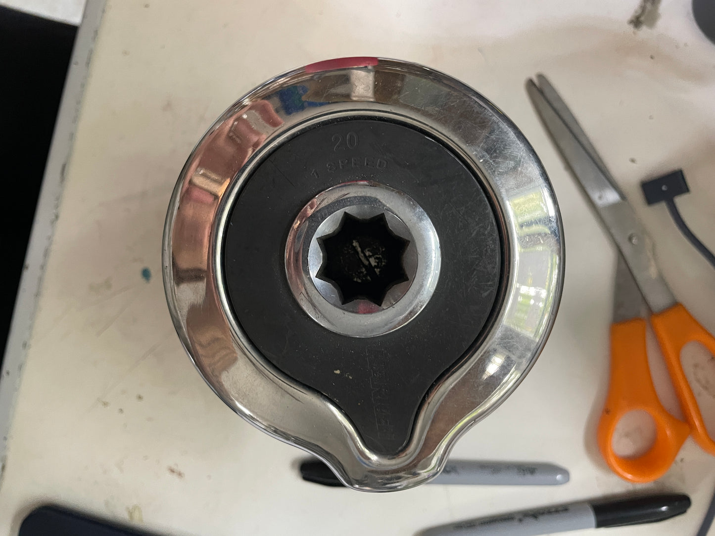 Metal tool bit on a white surface with scissors and pens in the background