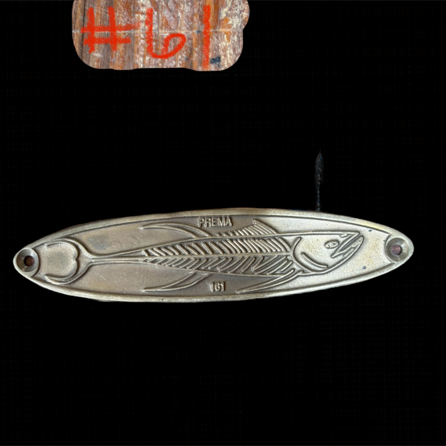 Metallic fish-shaped object with branding on a black background