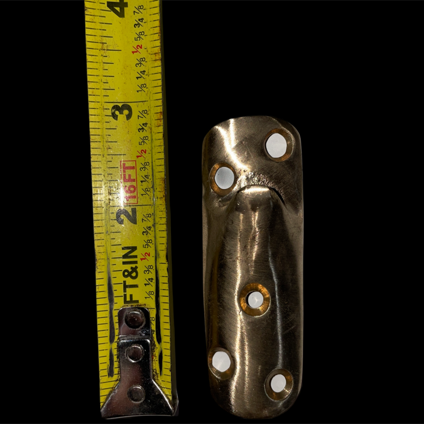 Metallic object with holes next to a measuring tape on a black background