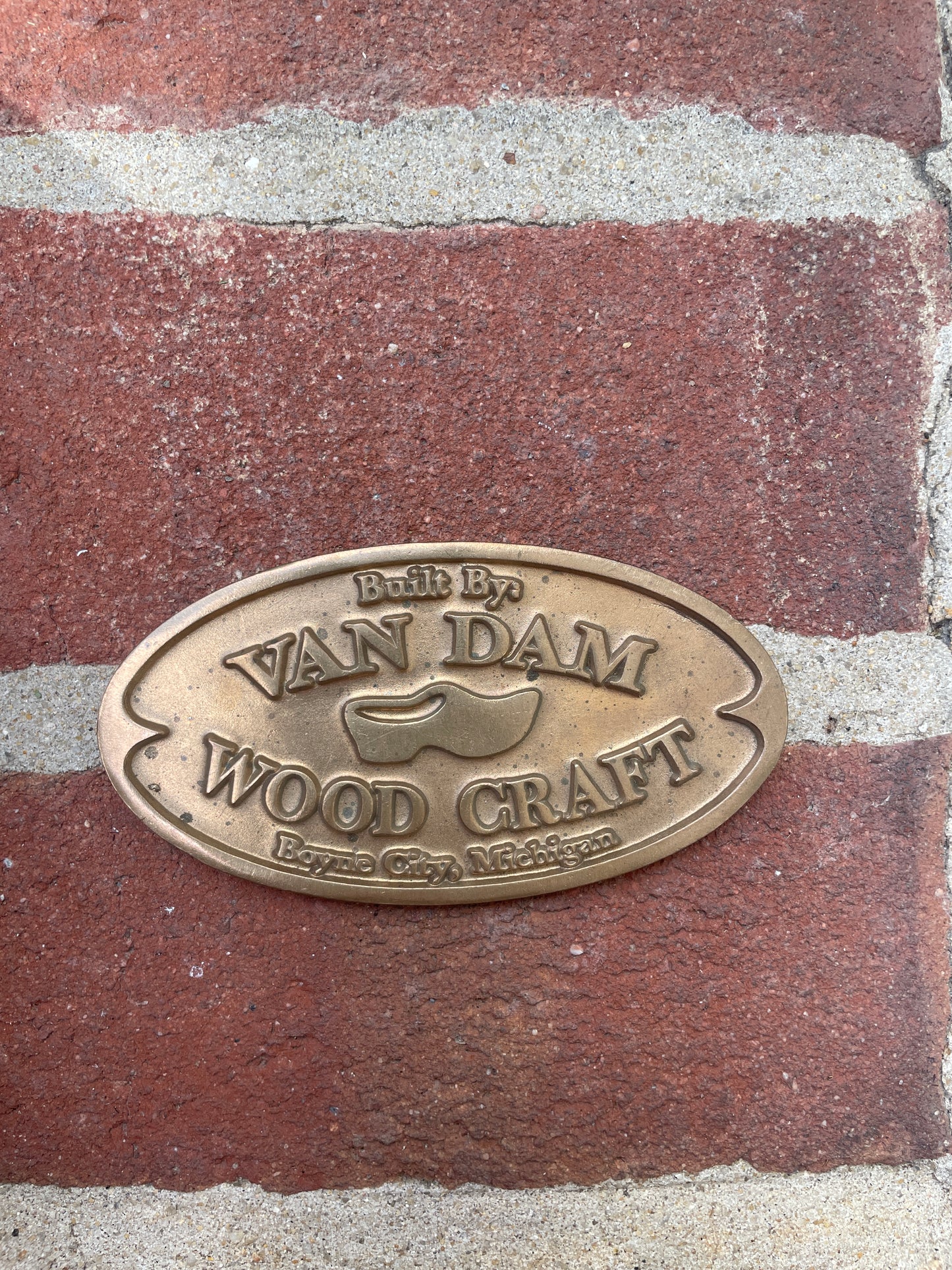 Bronze plaque with 'Van Dam Woodcraft' logo on a brick surface