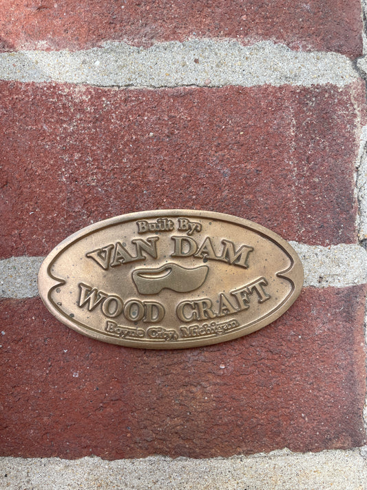 Bronze plaque with 'Van Dam Woodcraft' logo on a brick surface