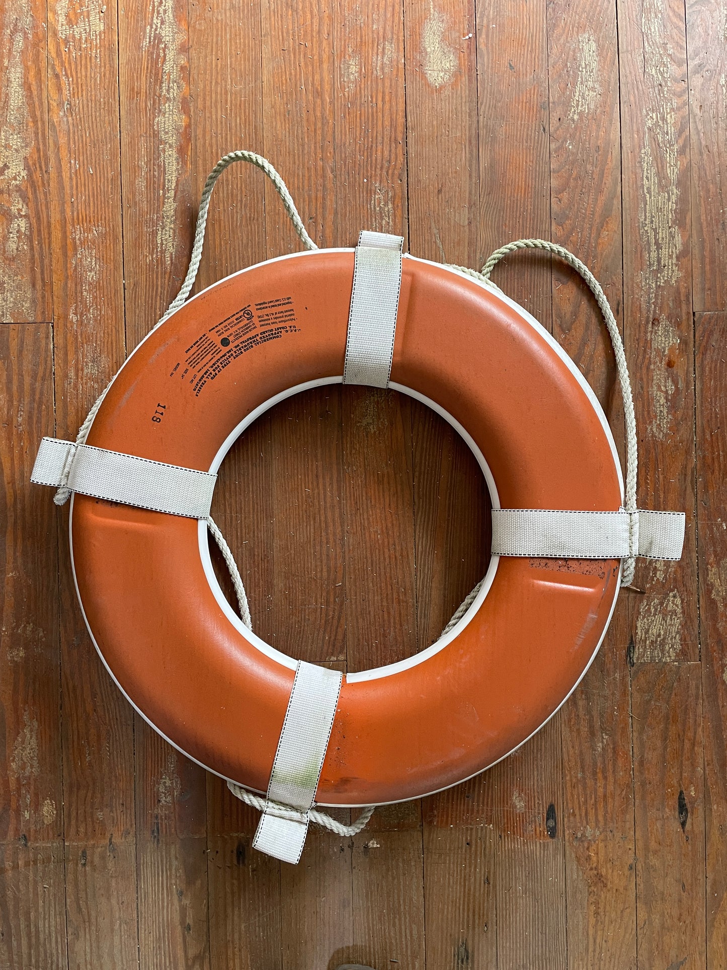 Orange life buoy with white straps on a wooden surface