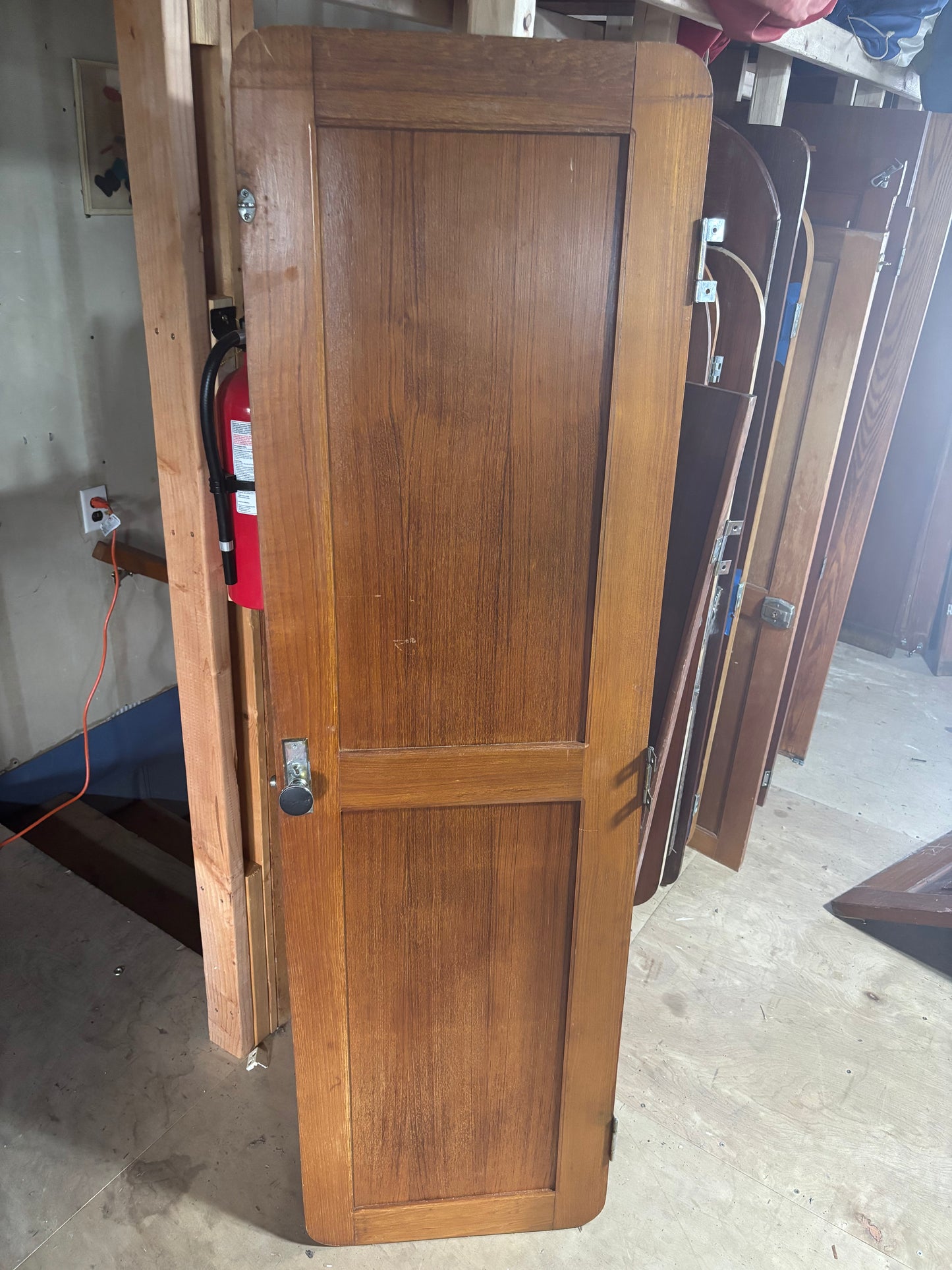 Wooden wardrobe in a storage or warehouse setting with other furniture items.