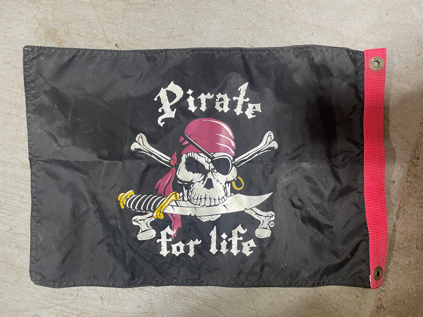 Black flag with pirate design and 'Pirate for life' text on a beige background