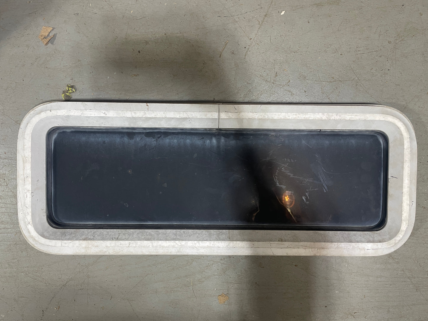 Rectangular black plastic component with white rim on a gray surface