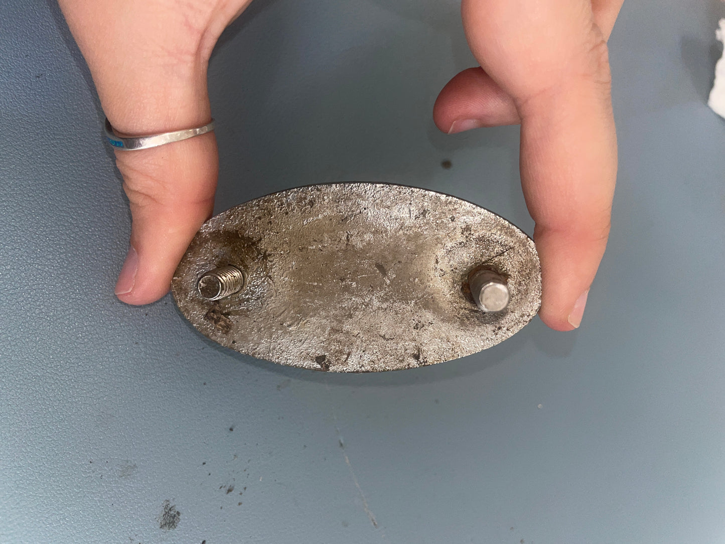Metal oval object held between two fingers against a gray background