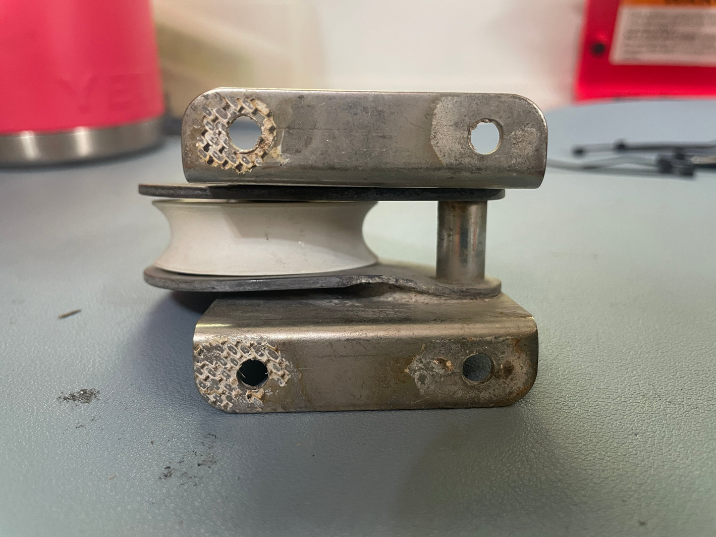 Metal pulley system on a gray surface with a red object in the background