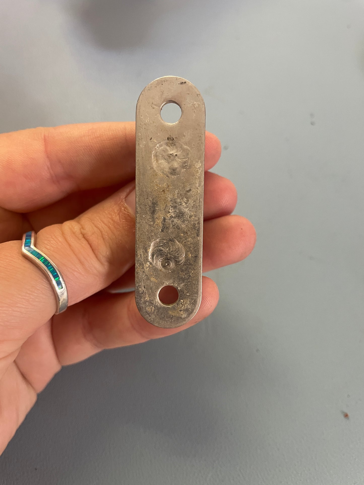Metal bracket held in a hand with a plain background