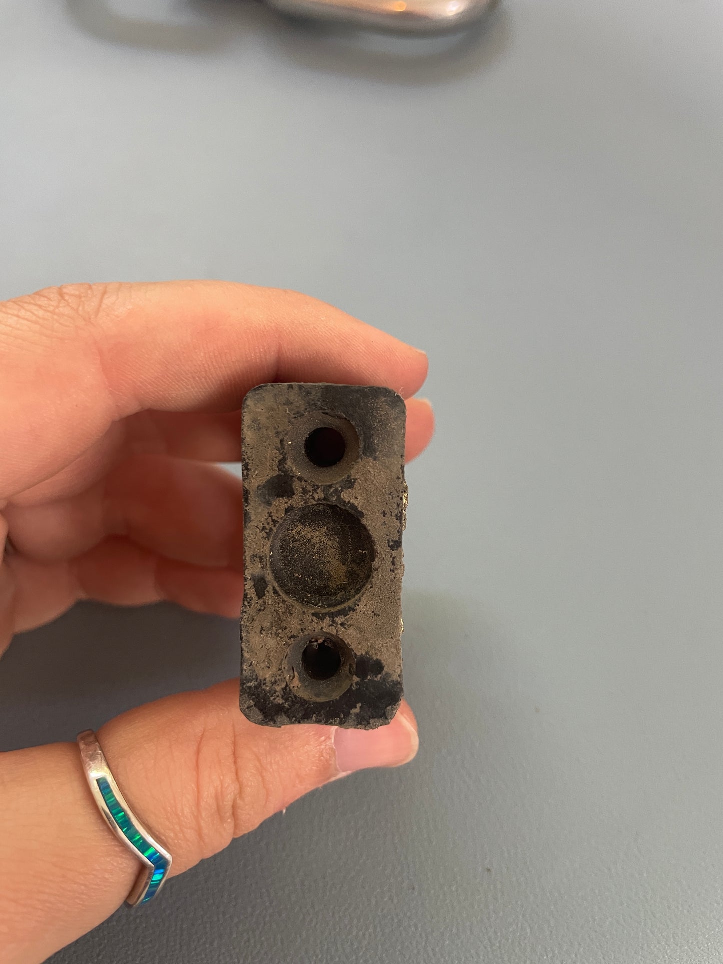 Hand holding a rectangular concrete block with two circular holes against a gray background