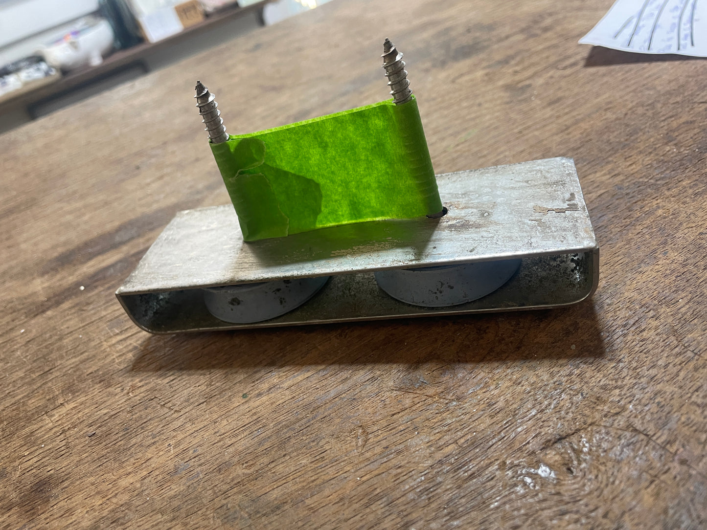 Small mechanical device with a green block and screws on a wooden surface