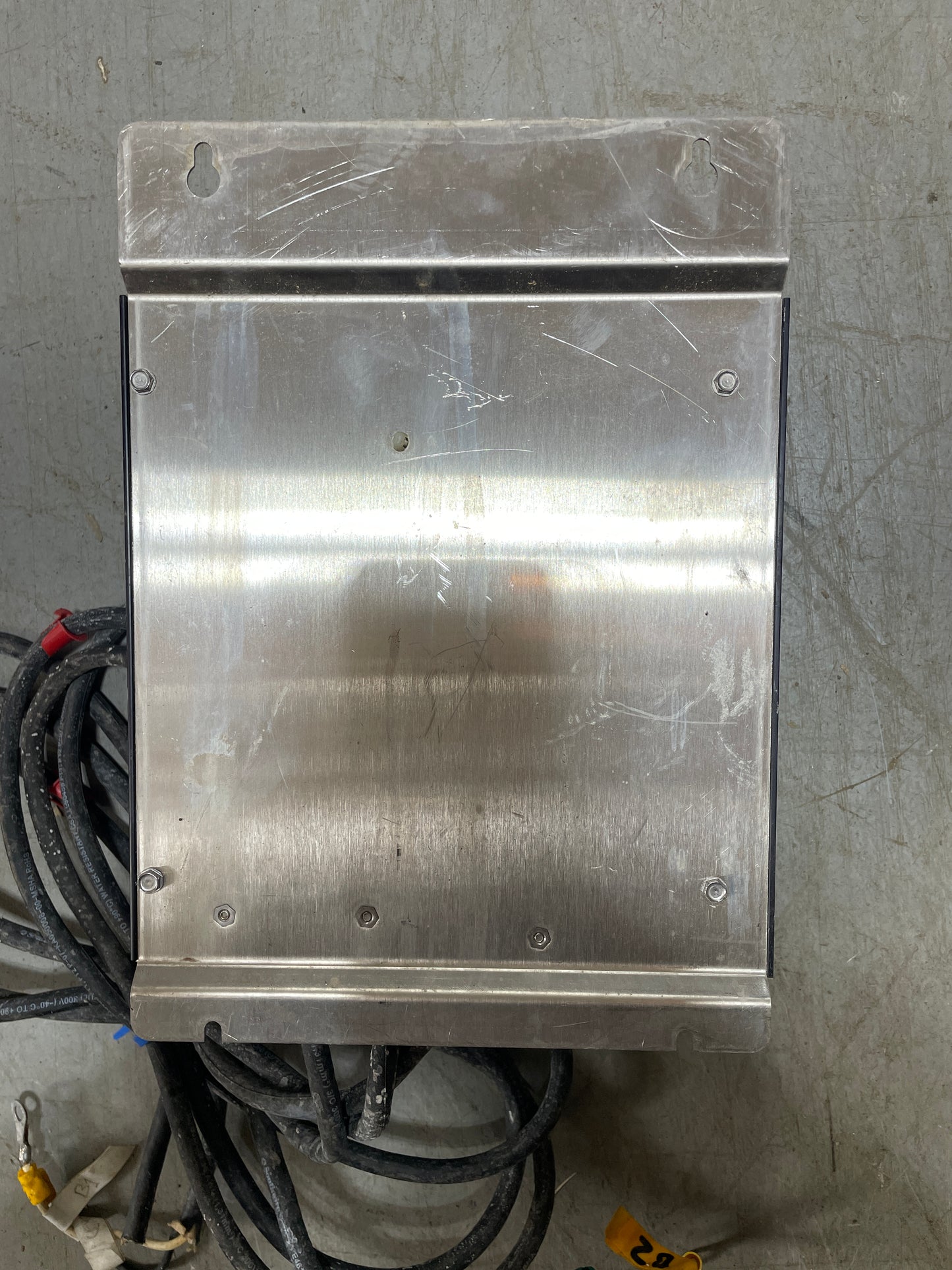 Metallic rectangular plate on a concrete floor with cables in the background