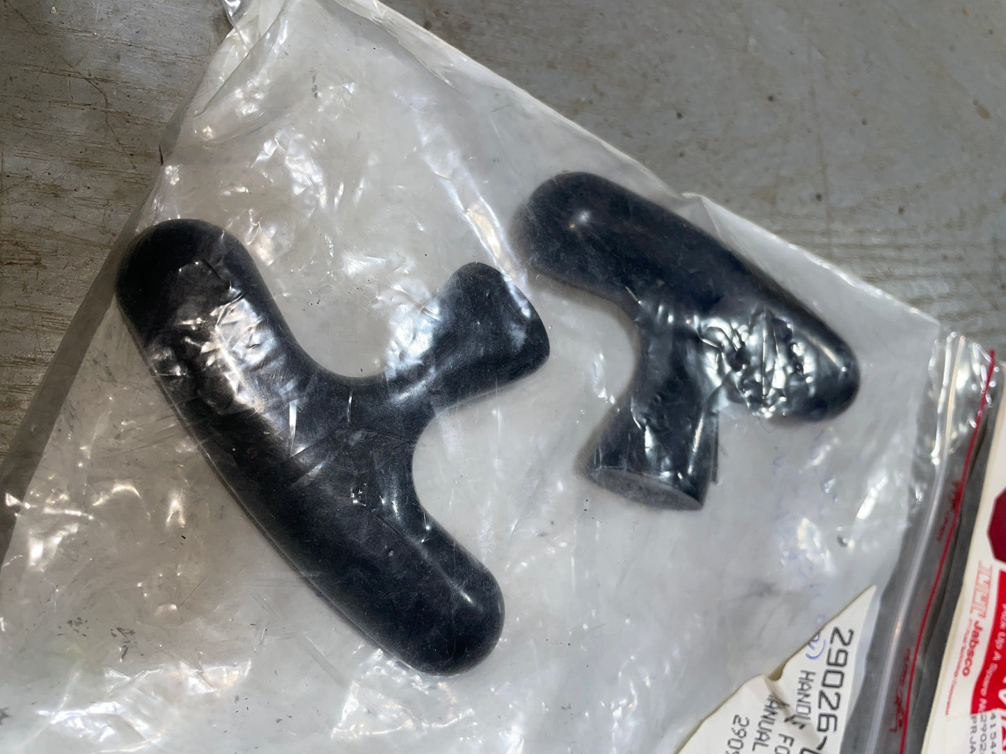 Two black plastic parts in a clear plastic bag on a metal surface.