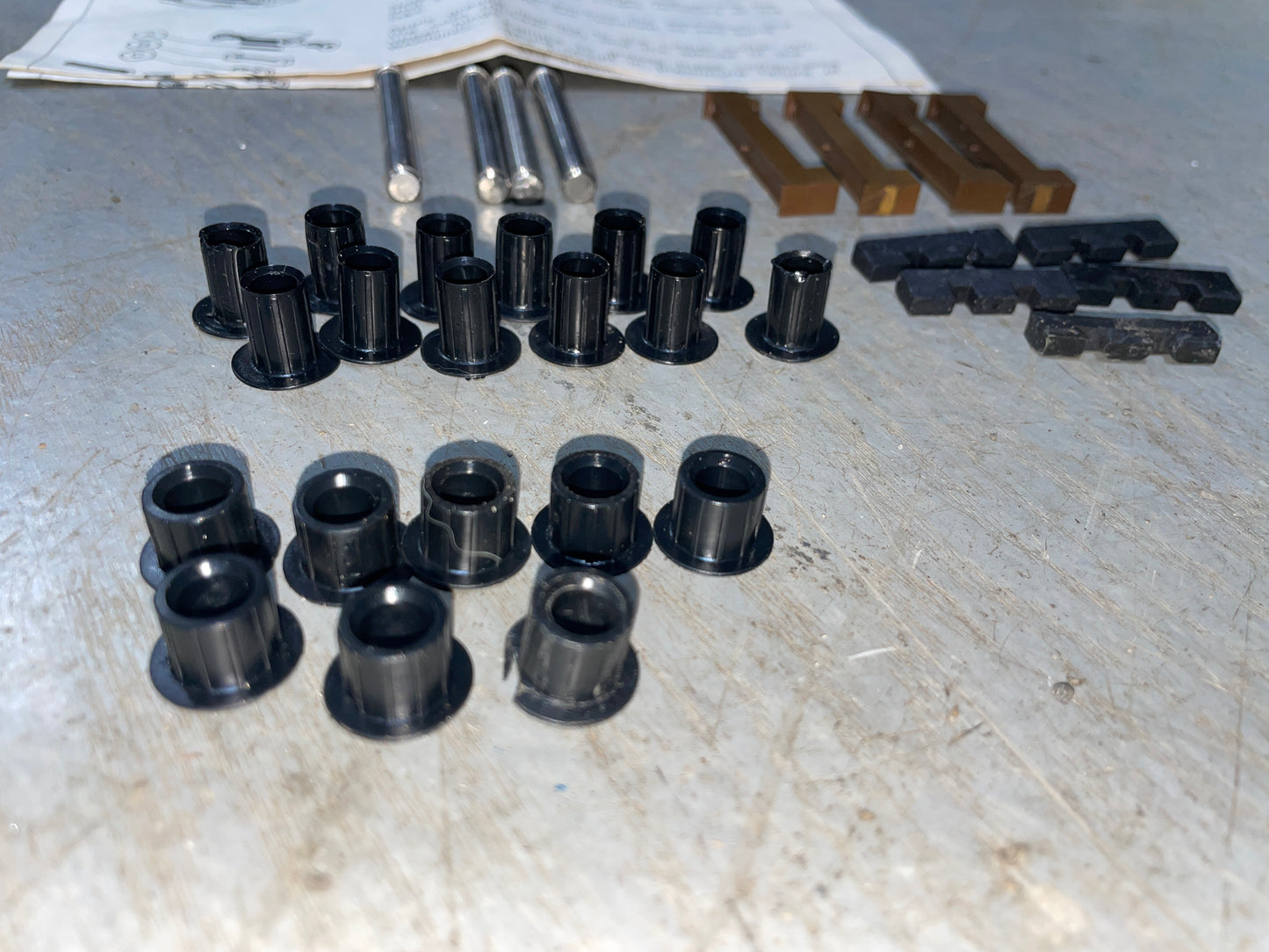 Collection of black metal bushings and other mechanical parts on a gray surface.