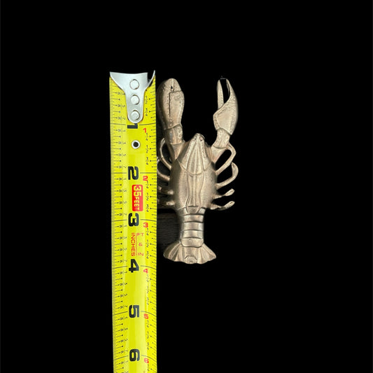 Metallic lobster-shaped object next to a measuring tape on a black background