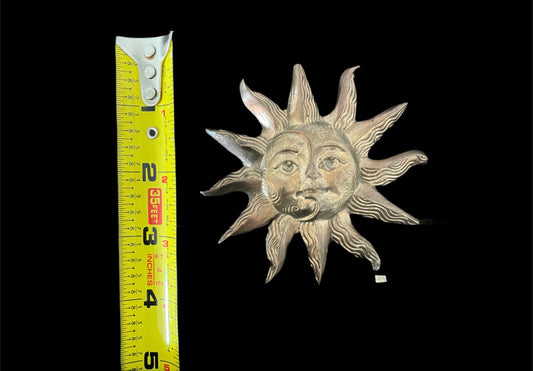 Decorative sun-shaped object with face next to a measuring tape on a black background