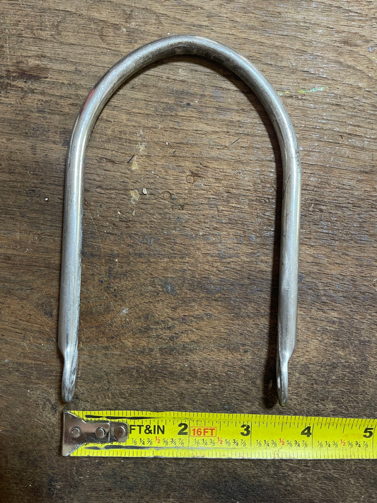 Metal U-shaped bracket on a wooden surface with a measuring tape for scale.