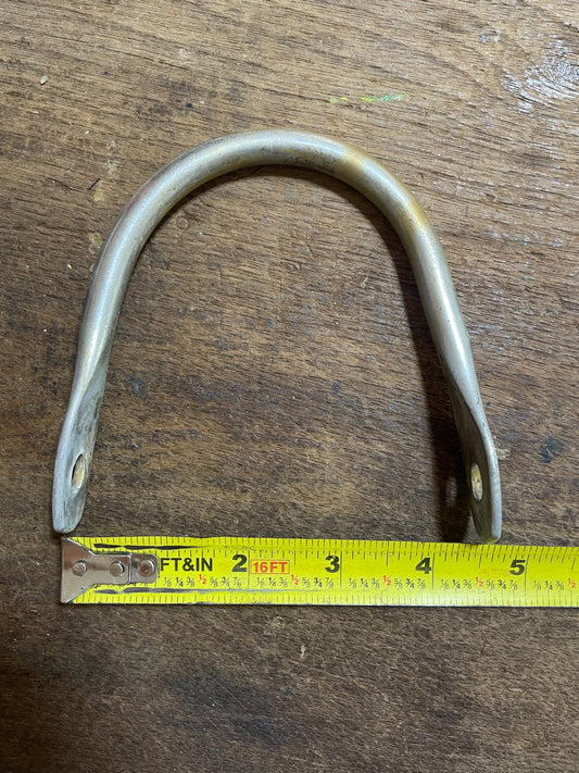 Metal U-shaped bracket on a wooden surface with a measuring tape for scale.
