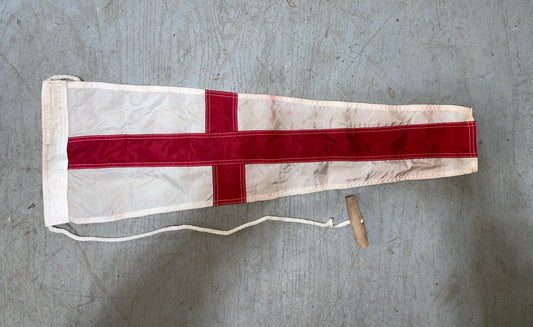 Flag with a red cross on a white background, attached to a wooden staff, on a gray surface.