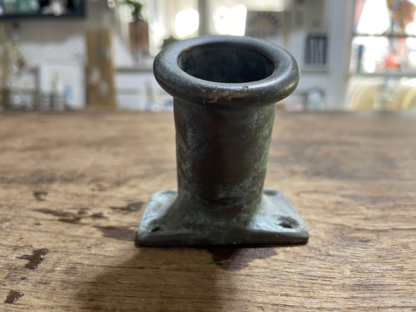 Metal pipe fitting on a wooden surface with a blurred indoor background