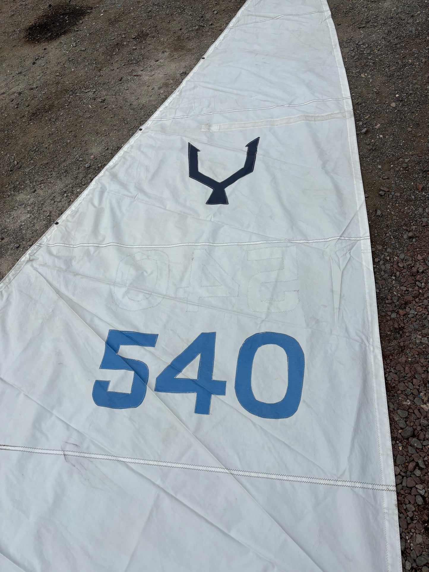 Close-up of a white sail with blue text and logo on a dark surface