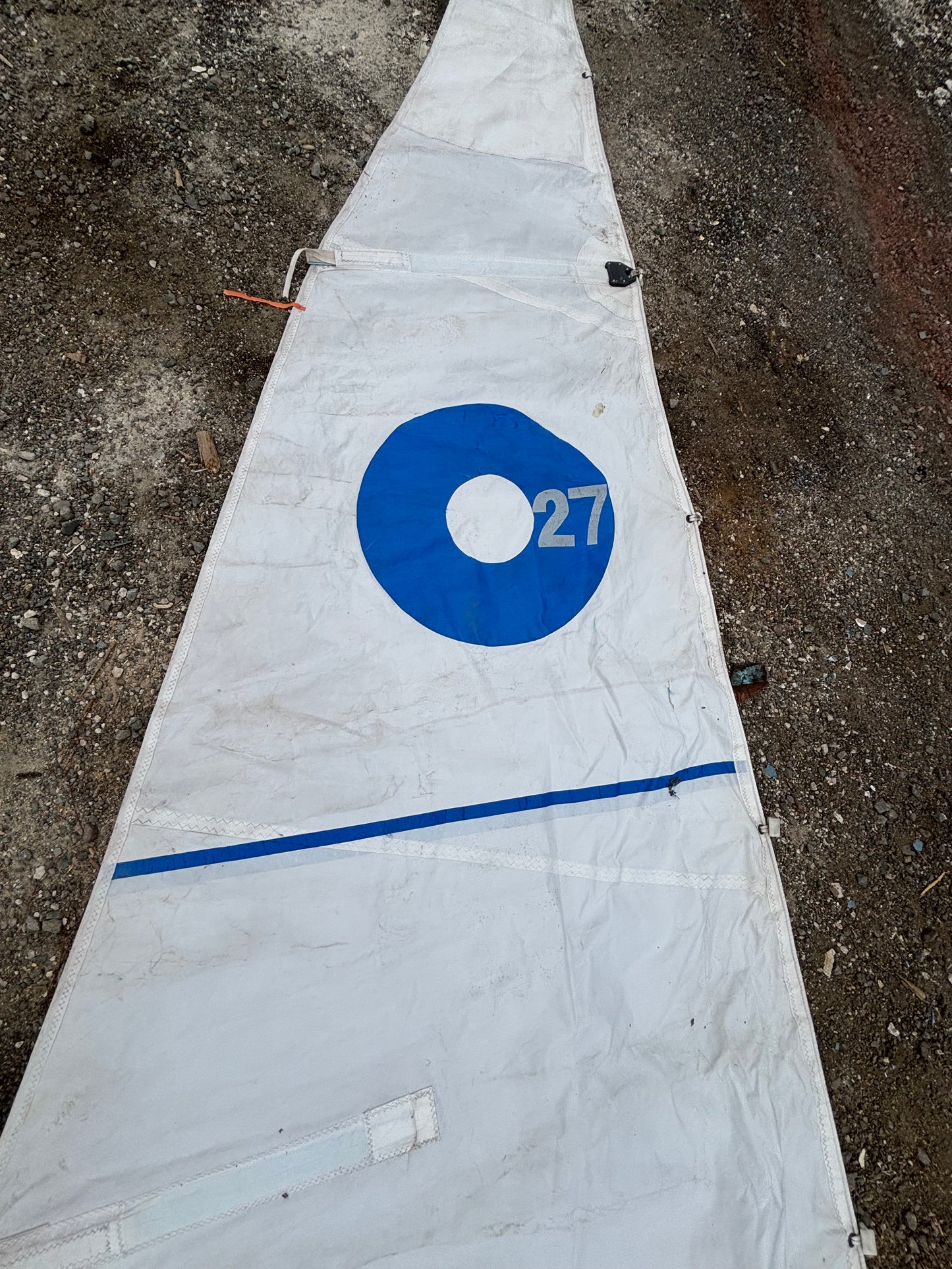 White sail with blue circle and number 27 on a textured surface