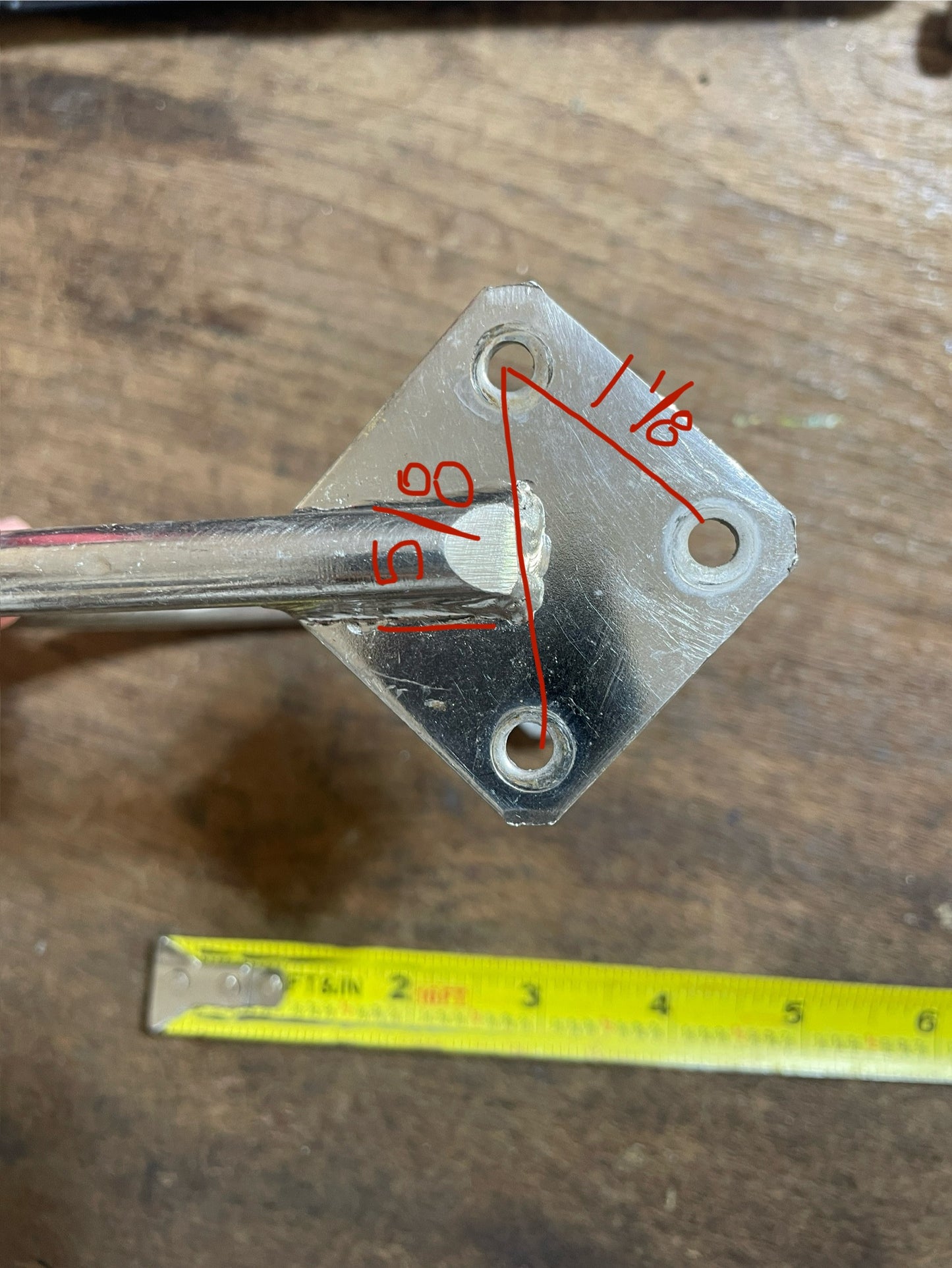 Metal bracket with measurements on a wooden surface, accompanied by a tape measure.