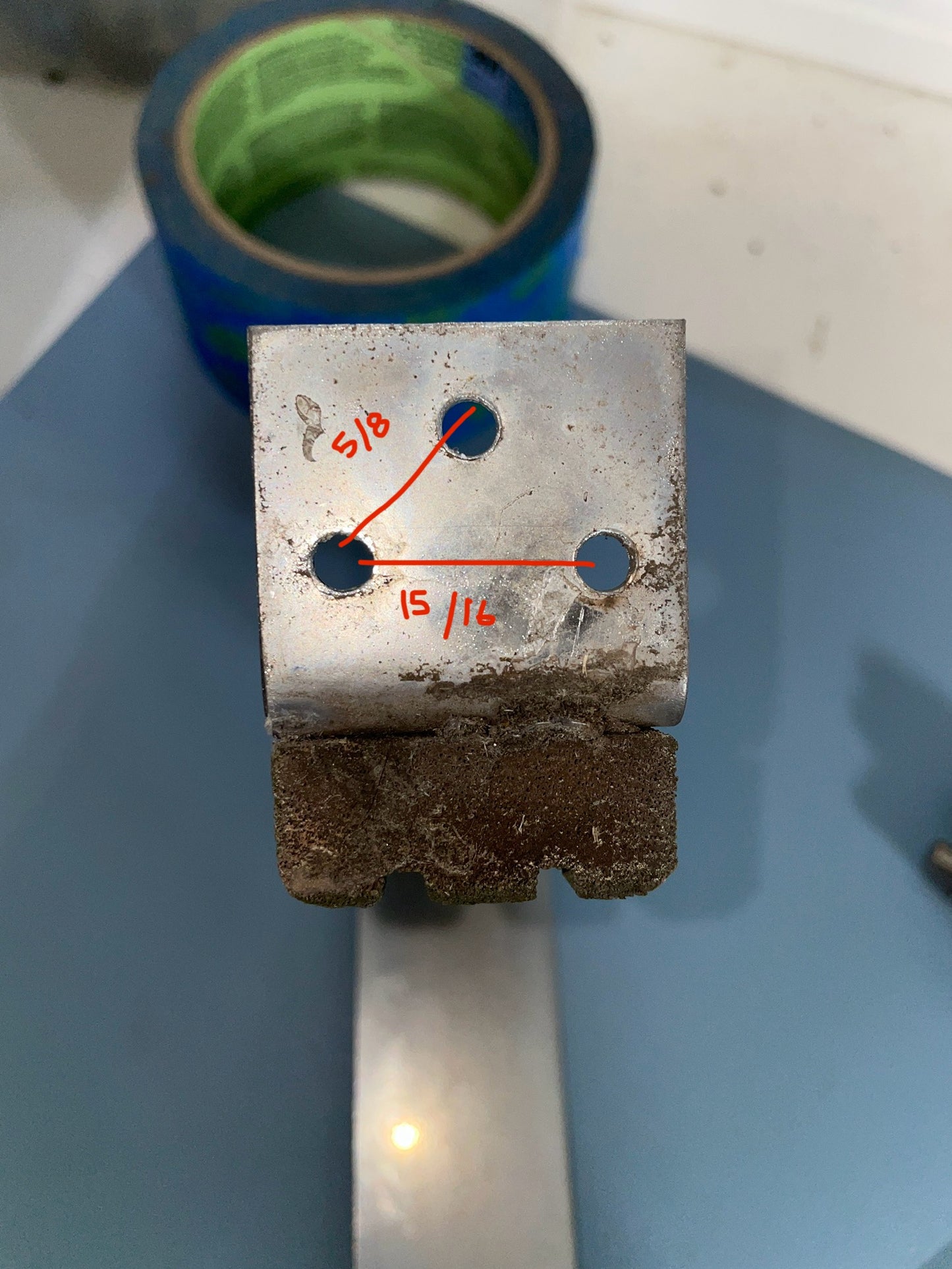 Metal component with measurements and a roll of blue tape in the background
