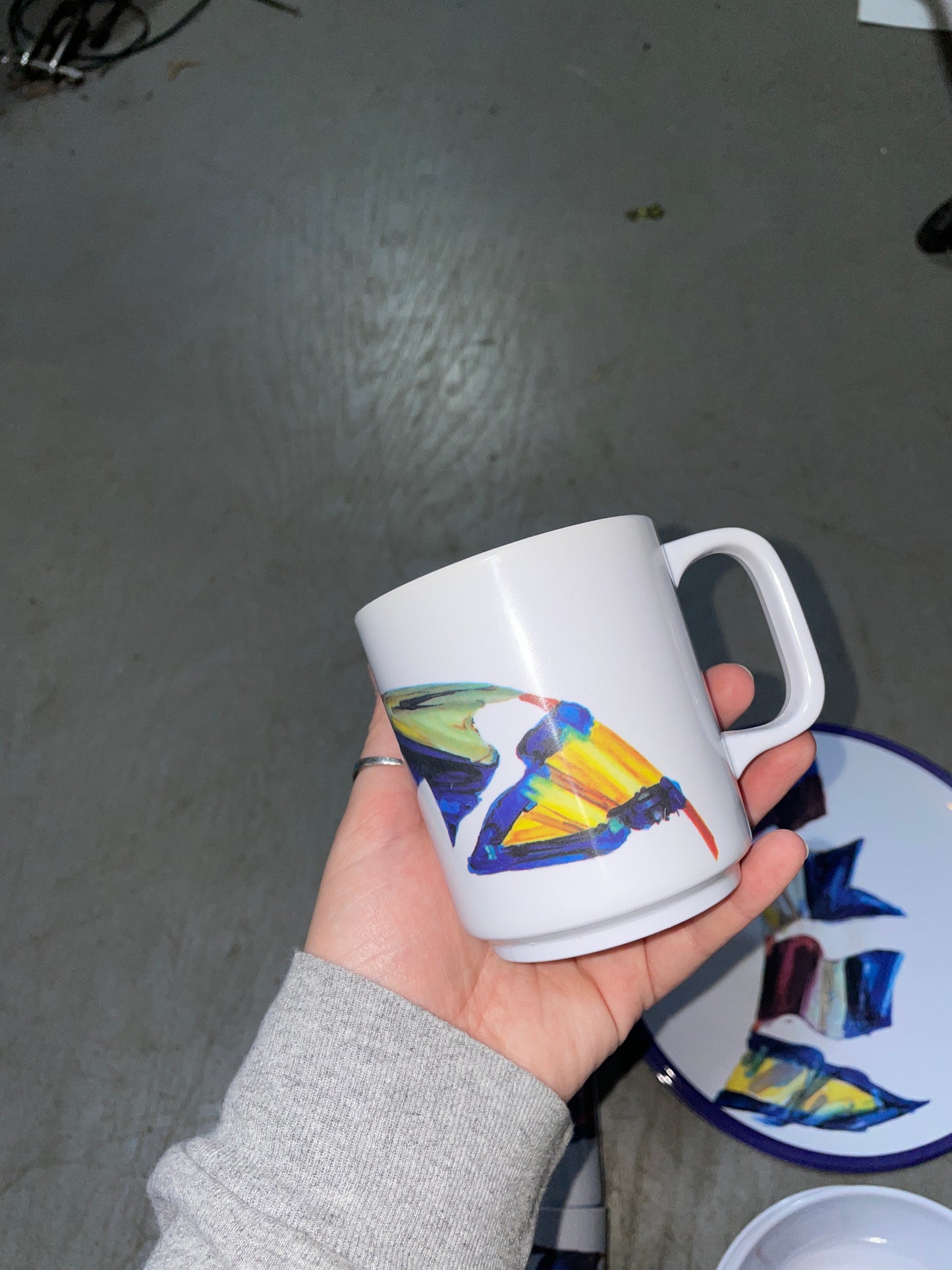 Hand holding a mug with a colorful design on a gray floor.
