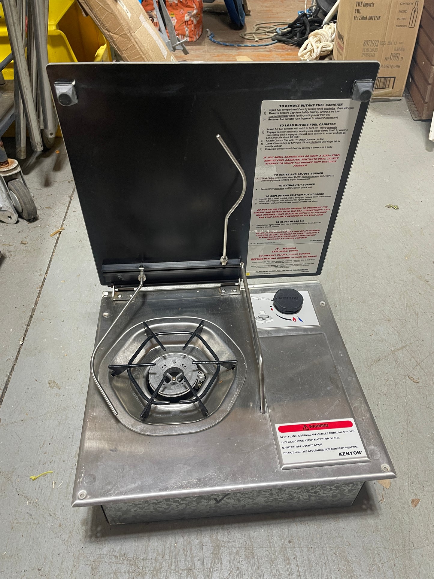 Portable gas stove with open lid on a concrete floor