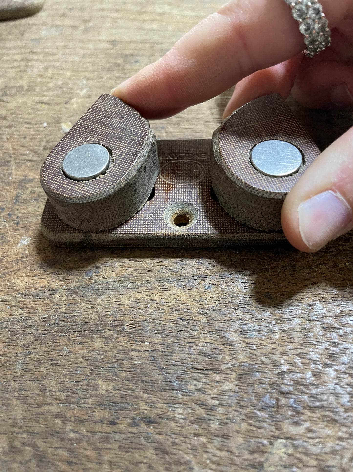 Close-up of a hand holding a magnetic strip with fabric backing on a wooden surface.