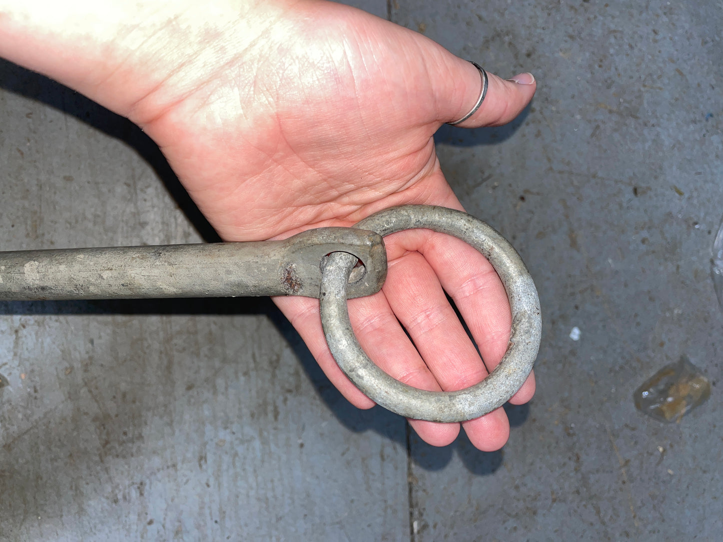 Metal ring and bar held by a hand against a concrete background