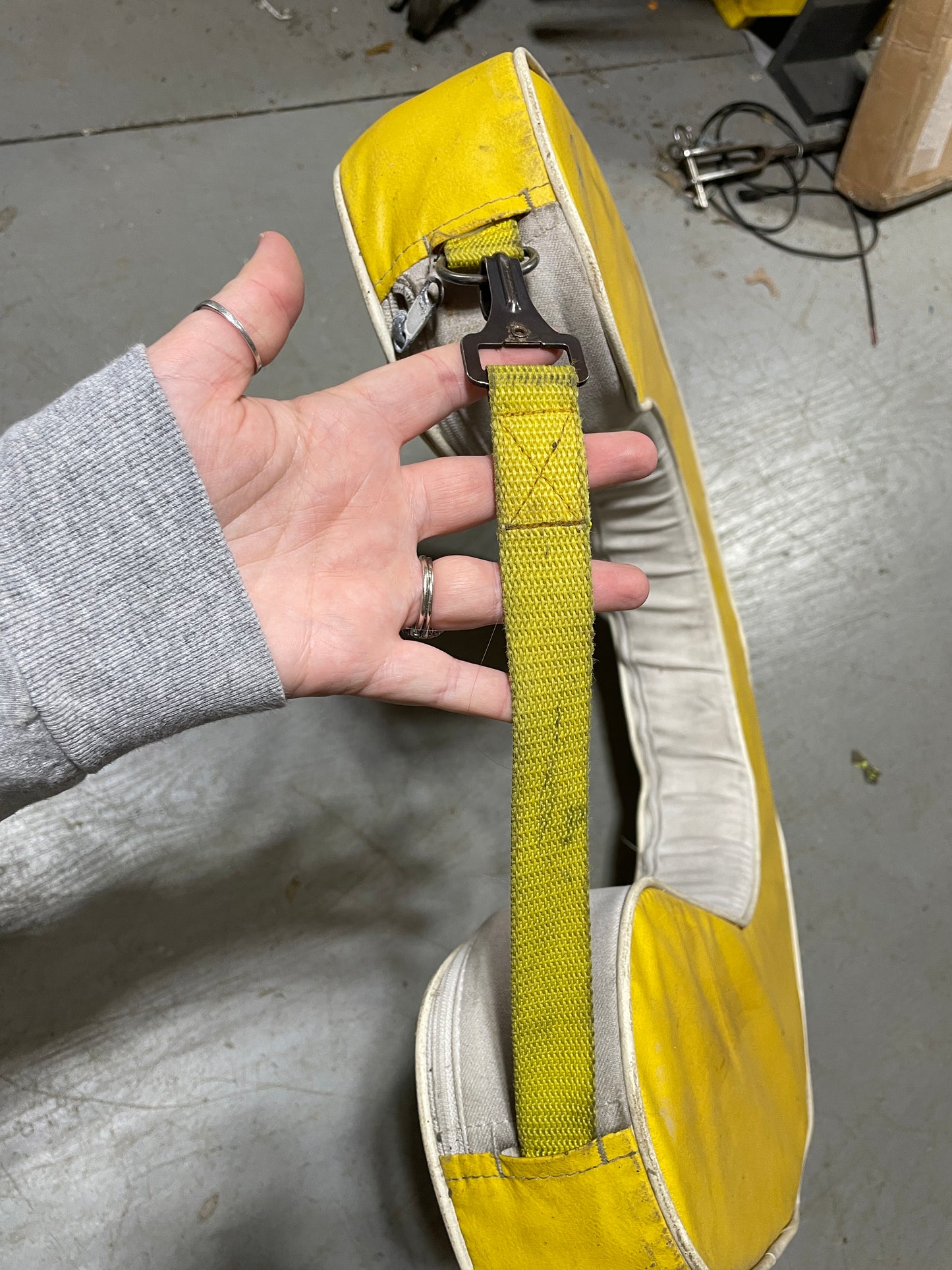 Hand holding a yellow strap over a large yellow and white object on a concrete floor.