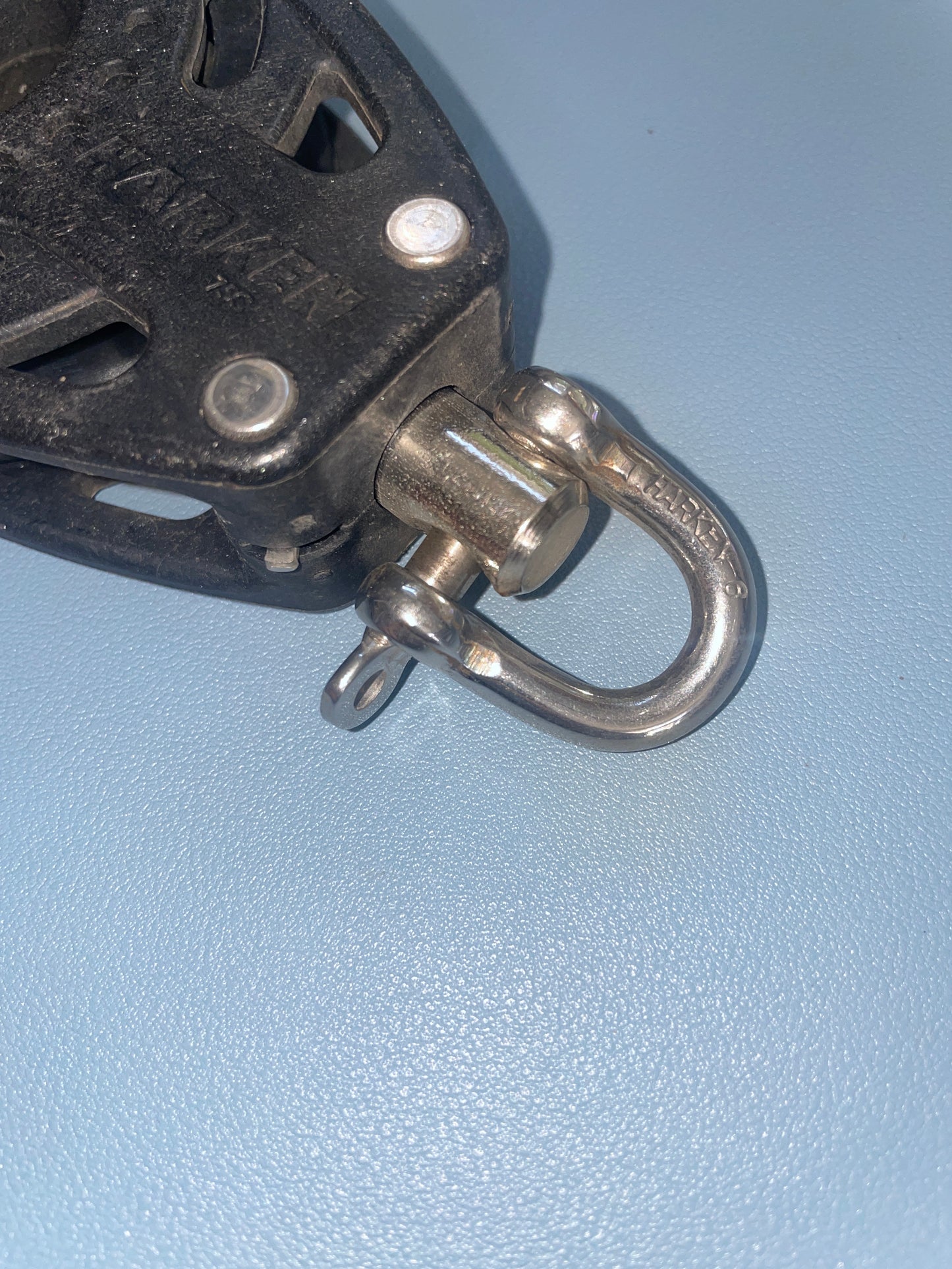 Metal hook attached to a black mechanical device on a light blue background