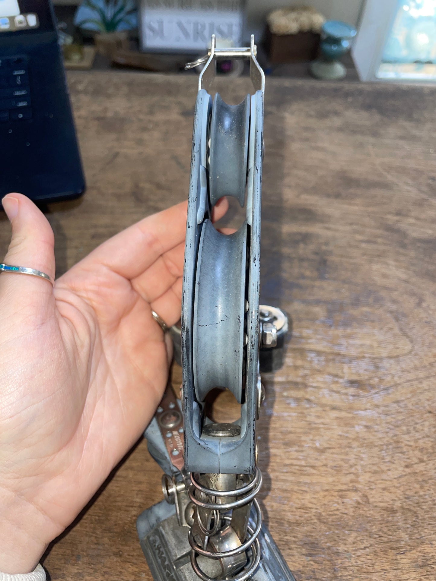 Metal pulley system held by a hand against a wooden background