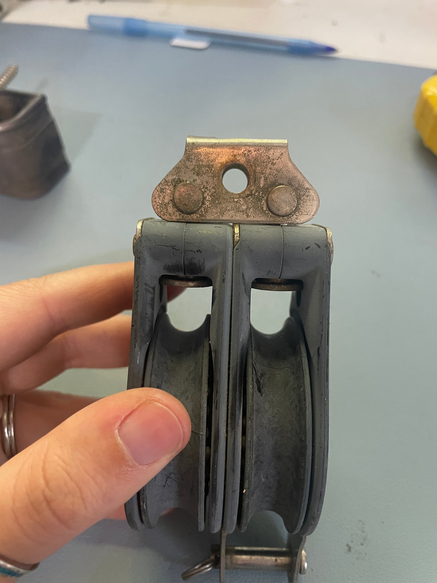 Hand holding a black metal component with a rusty hinge on a gray surface.