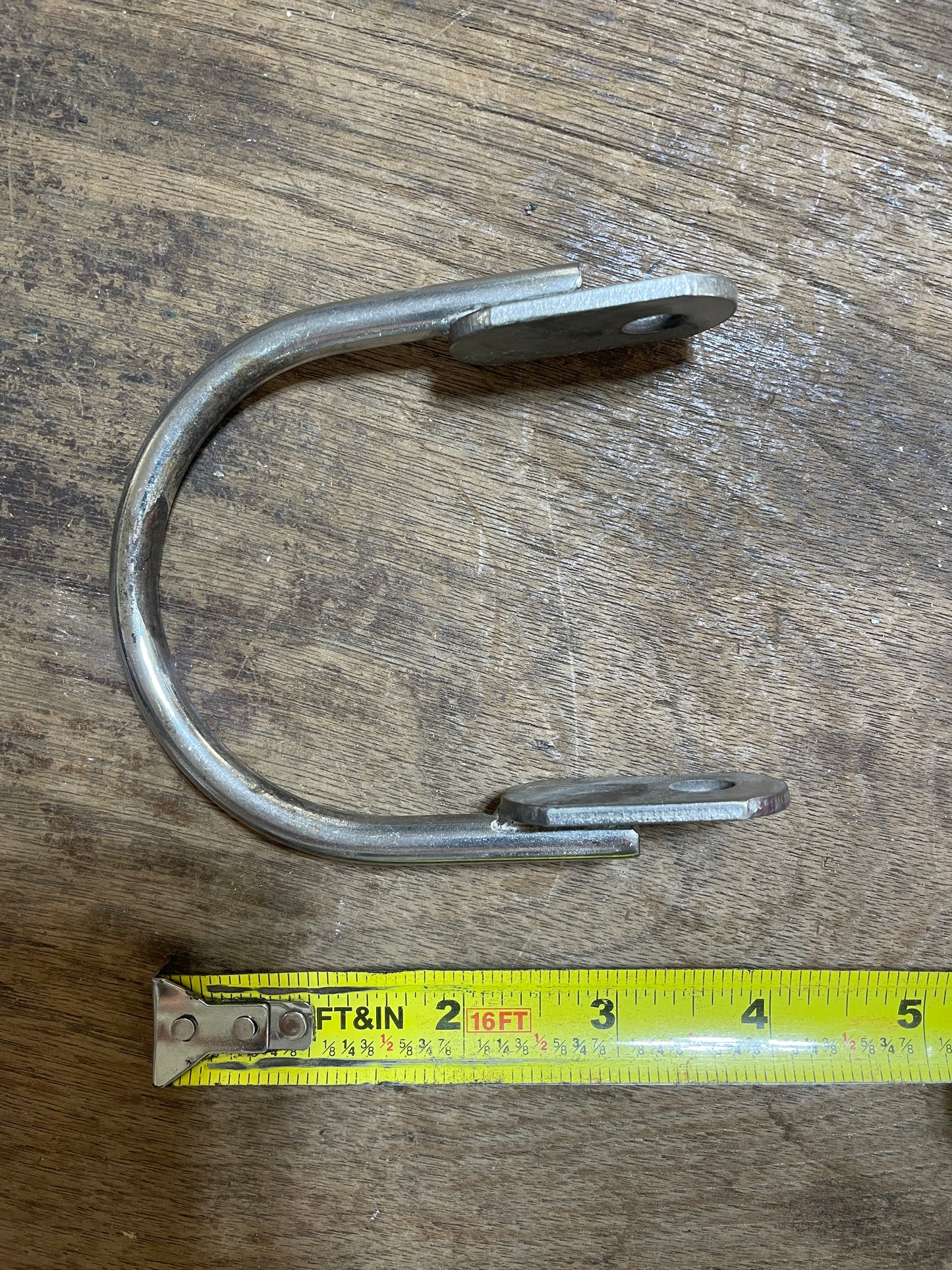 Metal U-shaped hook with measuring tape on a wooden surface