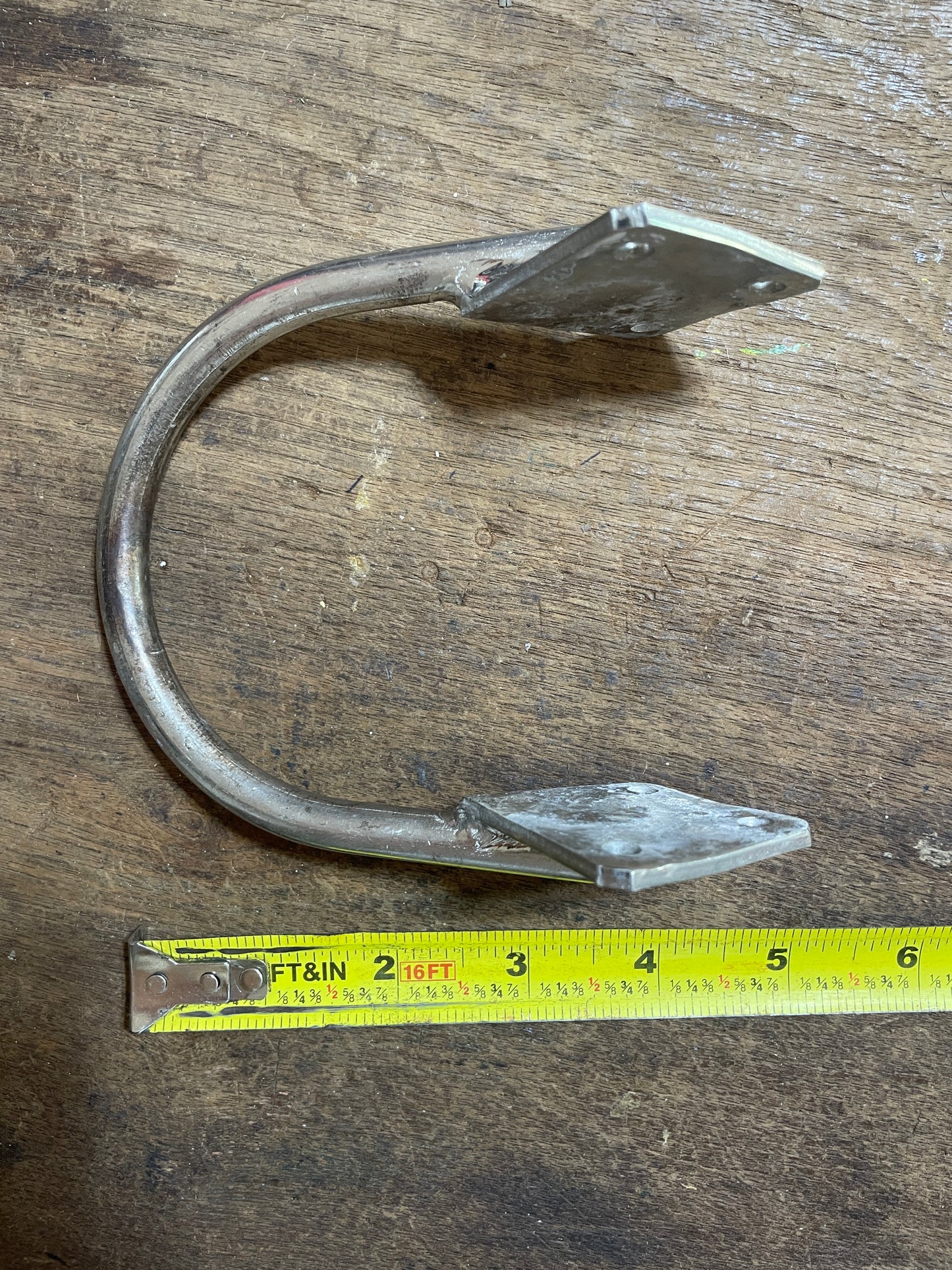Metal fish hook on a wooden surface with a measuring tape for scale.