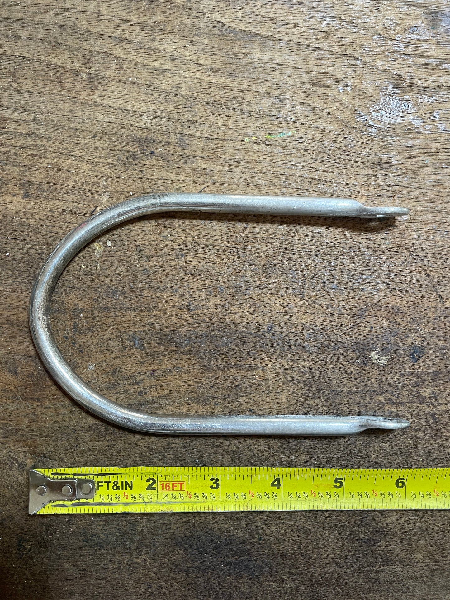Metal fish hook on a wooden surface with a measuring tape for scale.