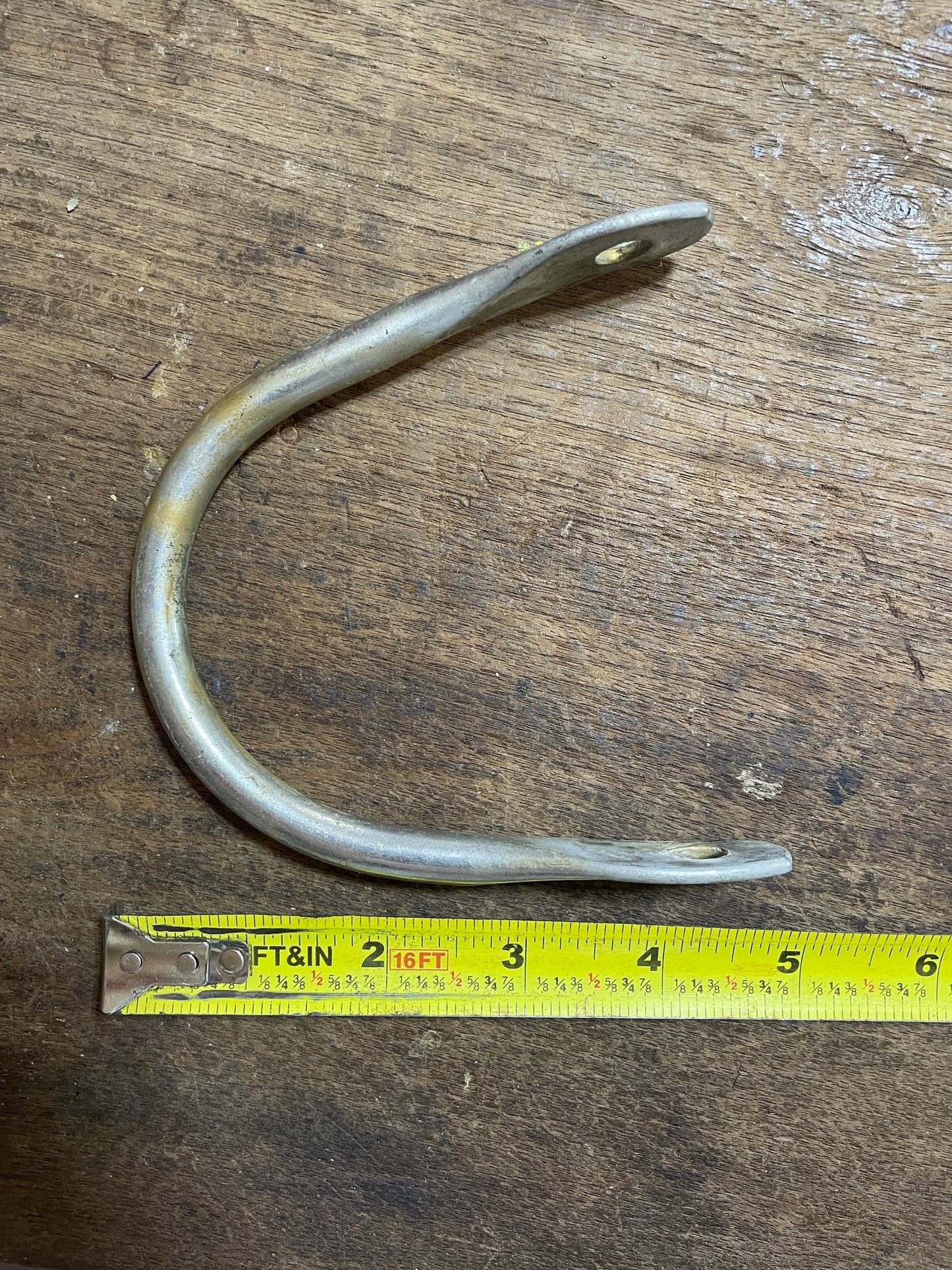 Metal U-shaped bracket on a wooden surface with a measuring tape for scale.
